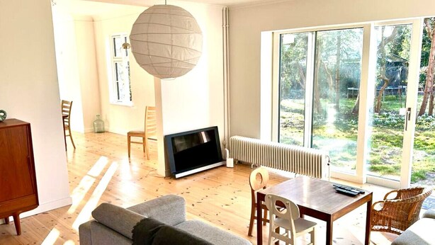 Een moderne woonkamer met een open haard, een eethoek en grote ramen met uitzicht op de omgeving.
