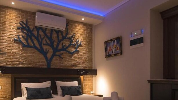 Een slaapkamer met een bakstenen muur, een decoratie in de vorm van een boom, een bed met kussens en een nachtkastje.