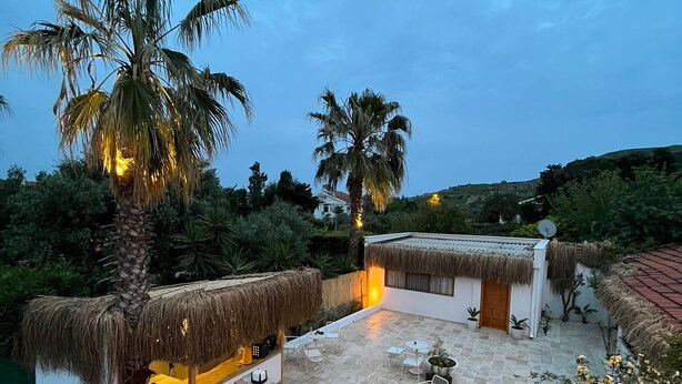 A rooftop patio with thatched-roof structures, outdoor seating, and palm trees. - kai urla (Urla)
