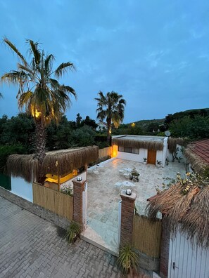 A rooftop patio with thatched-roof structures, outdoor seating, and palm trees. - kai urla (Urla)