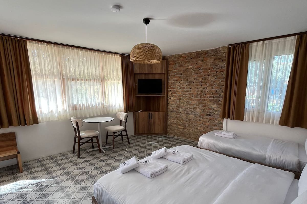 A hotel room with two beds, a desk, a chair, a TV, and a patterned floor.