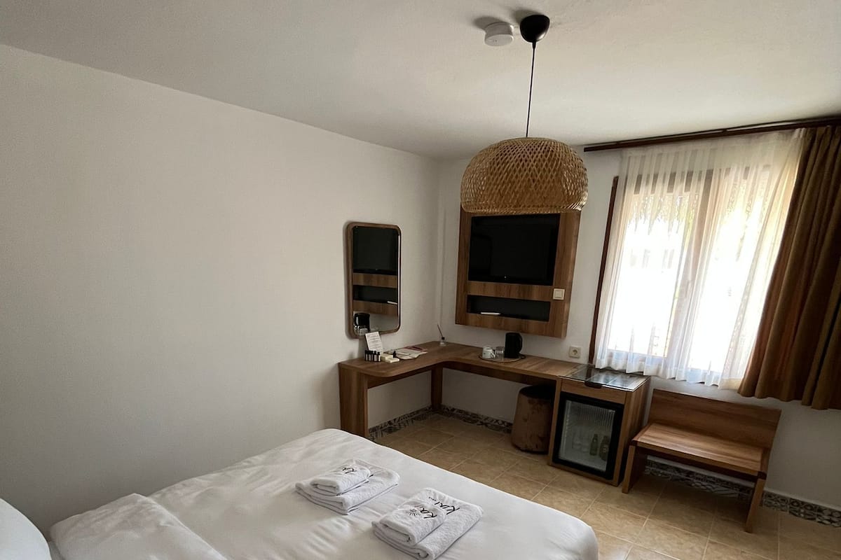 A hotel room with a bed, a desk with a computer, a television, and a window with curtains.