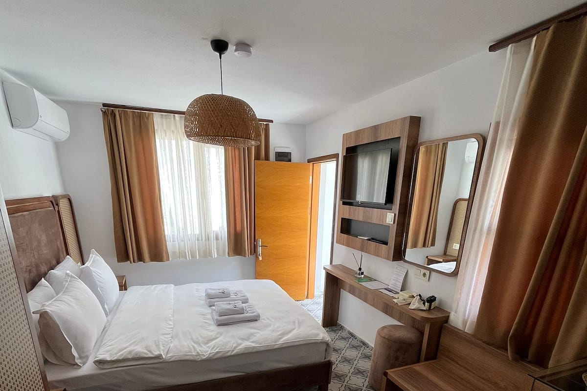 A hotel room with a large bed, a TV, a desk with a mirror, and a patterned floor.
