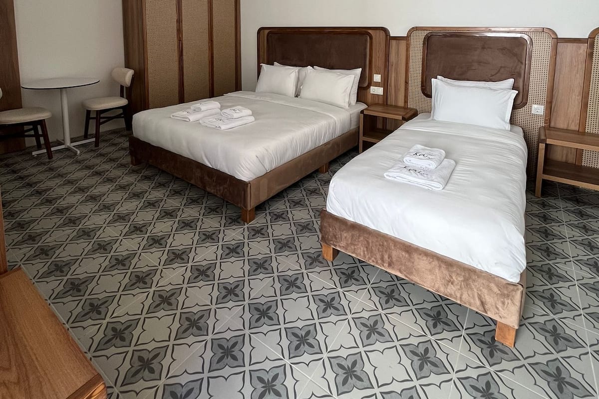 A hotel room with two beds, a small table, and a chair.