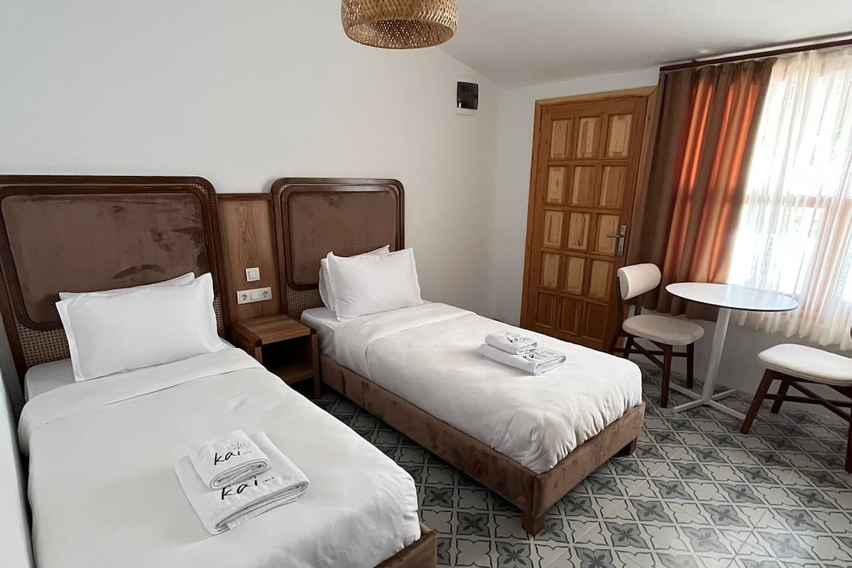 A hotel room with two beds, a small table, and a chair.