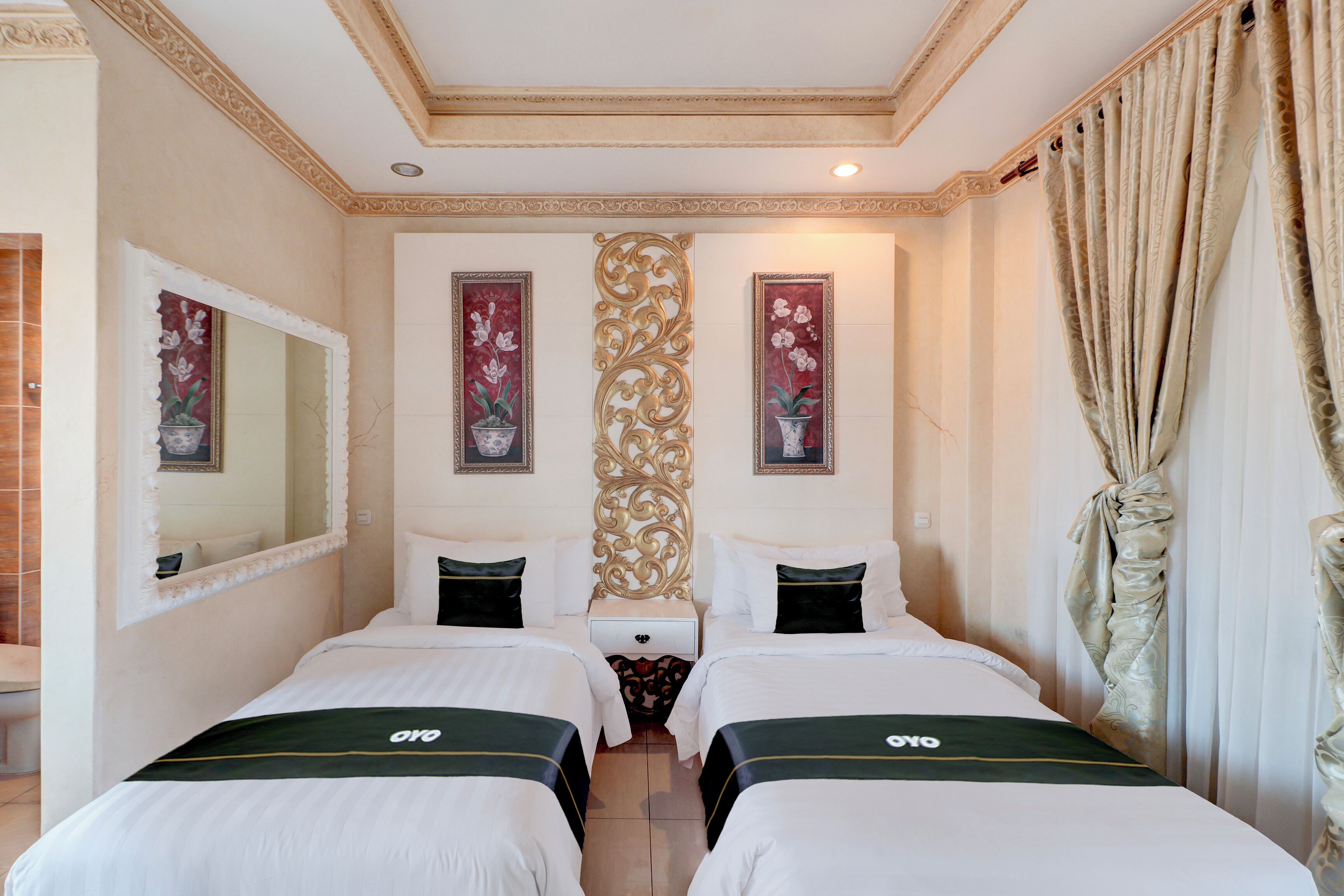 A hotel room with two beds, a large mirror, decorative wall panels, and a window with curtains.