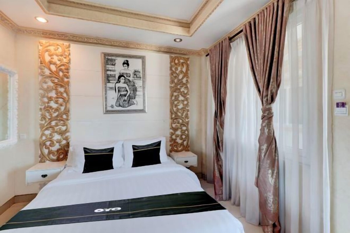 A hotel room with a large bed, two bedside tables, a wall-mounted artwork, and a window with curtains.