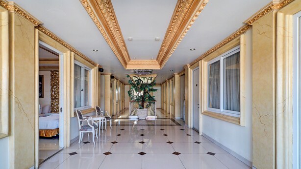 A hotel corridor with a marble floor, ornate ceiling, and a central plant. - Hotel O My Home@Bali (Kuta)