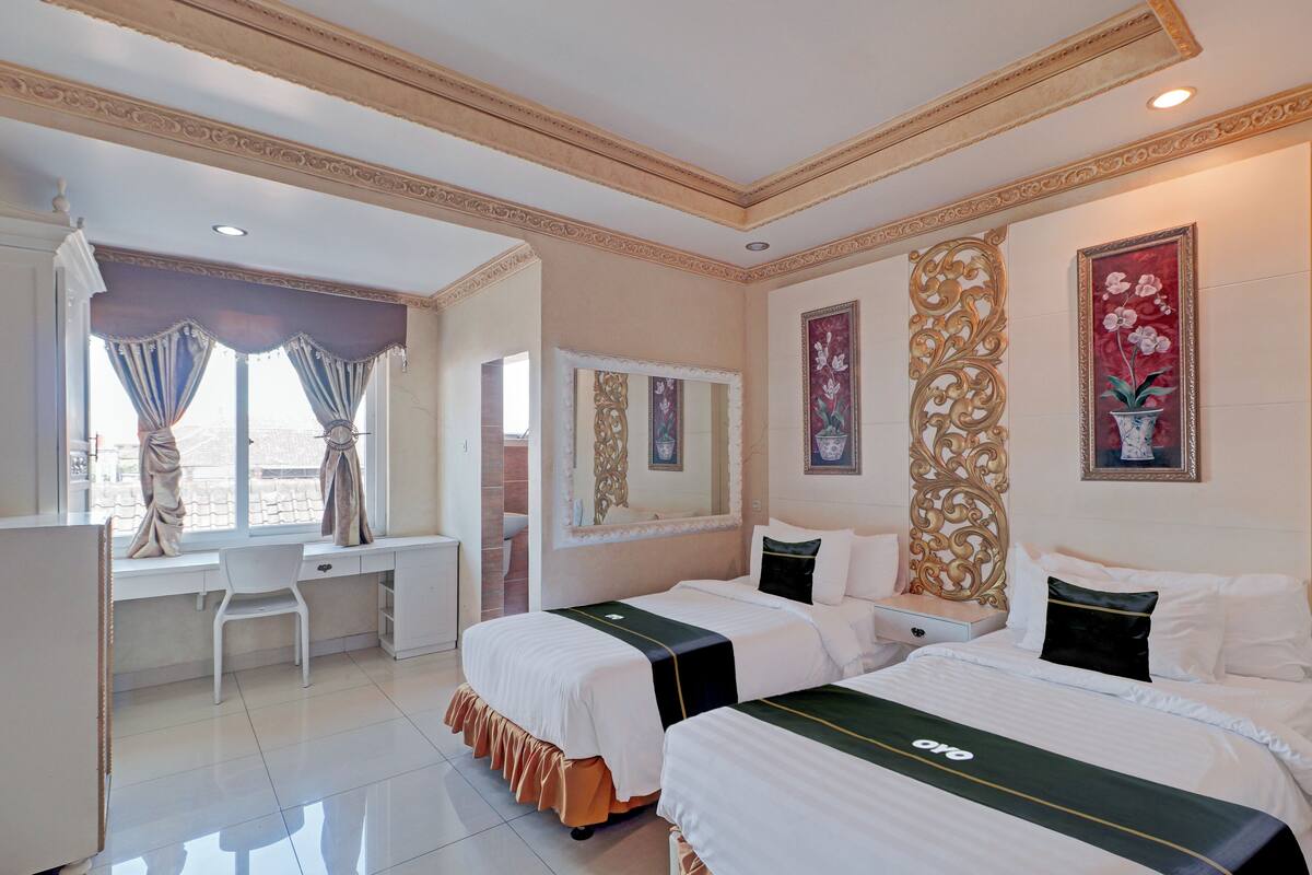 A hotel room with two beds, a desk, a chair, and a large window with curtains.