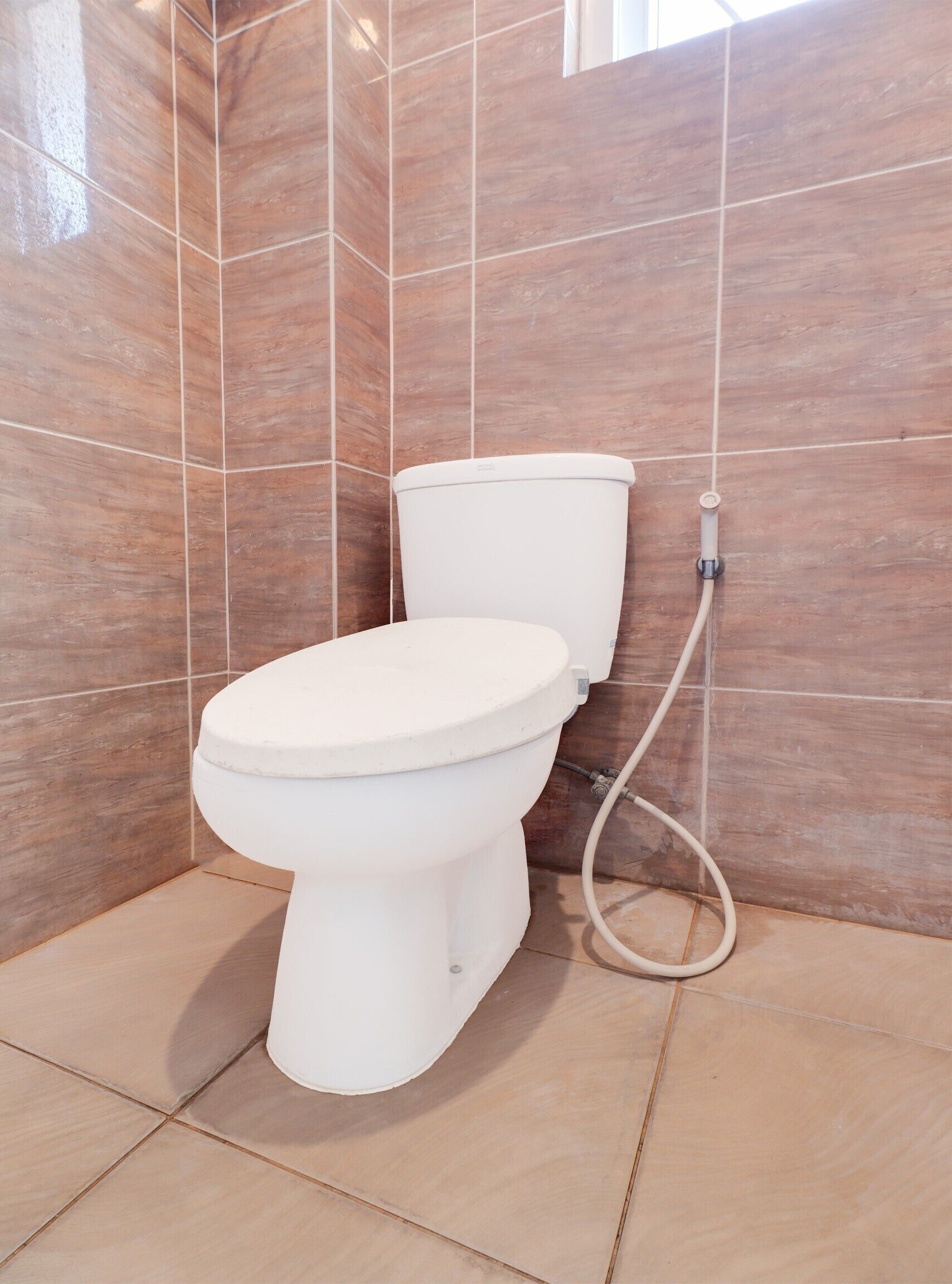 Un baño moderno con inodoro blanco, azulejos color beige y una tubería de agua a la vista.