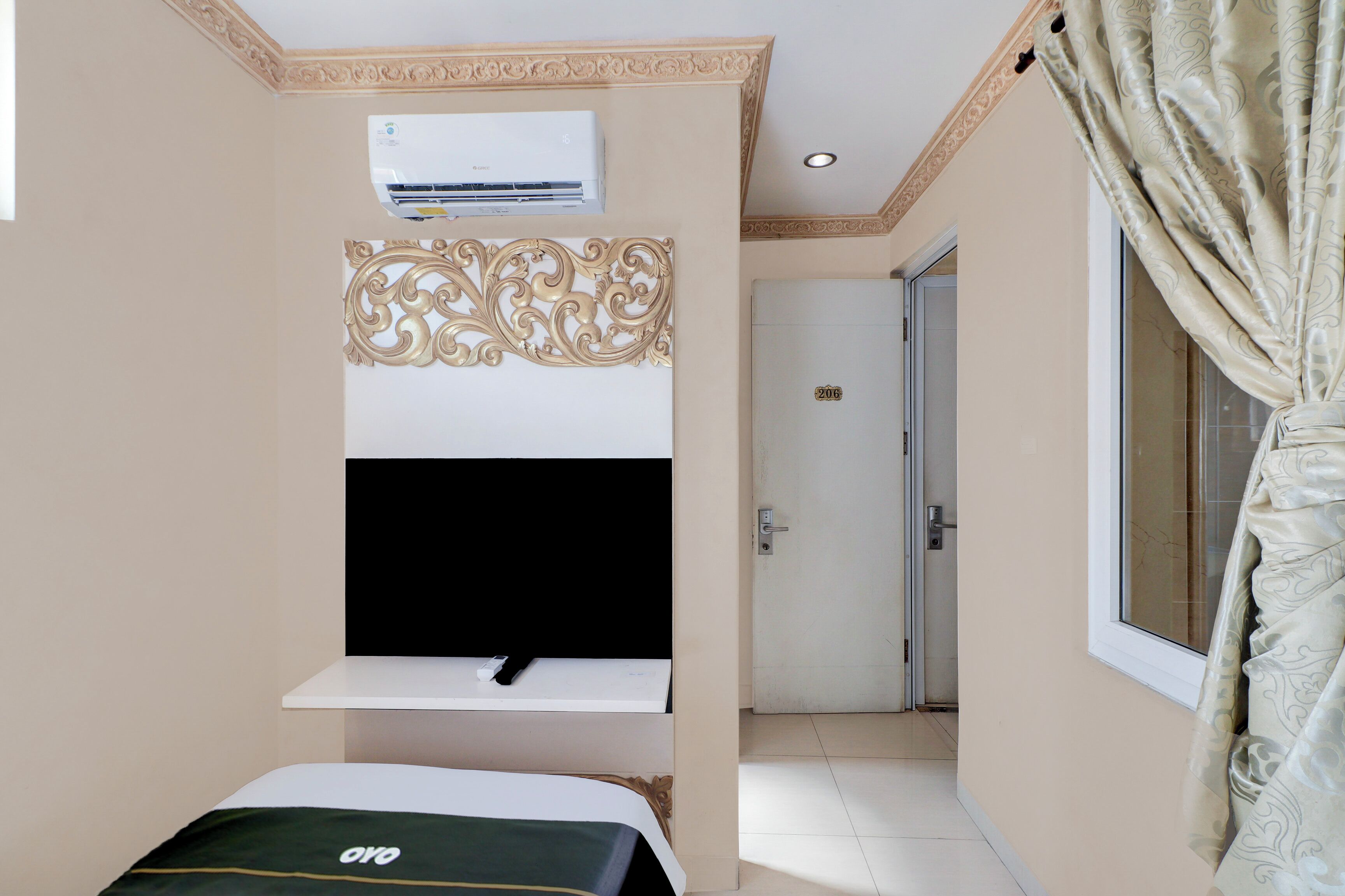 Habitación de hotel con cama, televisor montado, equipo de aire acondicionado, puerta y ventana con cortinas.