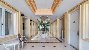 A hallway with a marble floor, a potted tree, and a seating area with a table and chairs. - Hotel O My Home@Bali (Kuta)