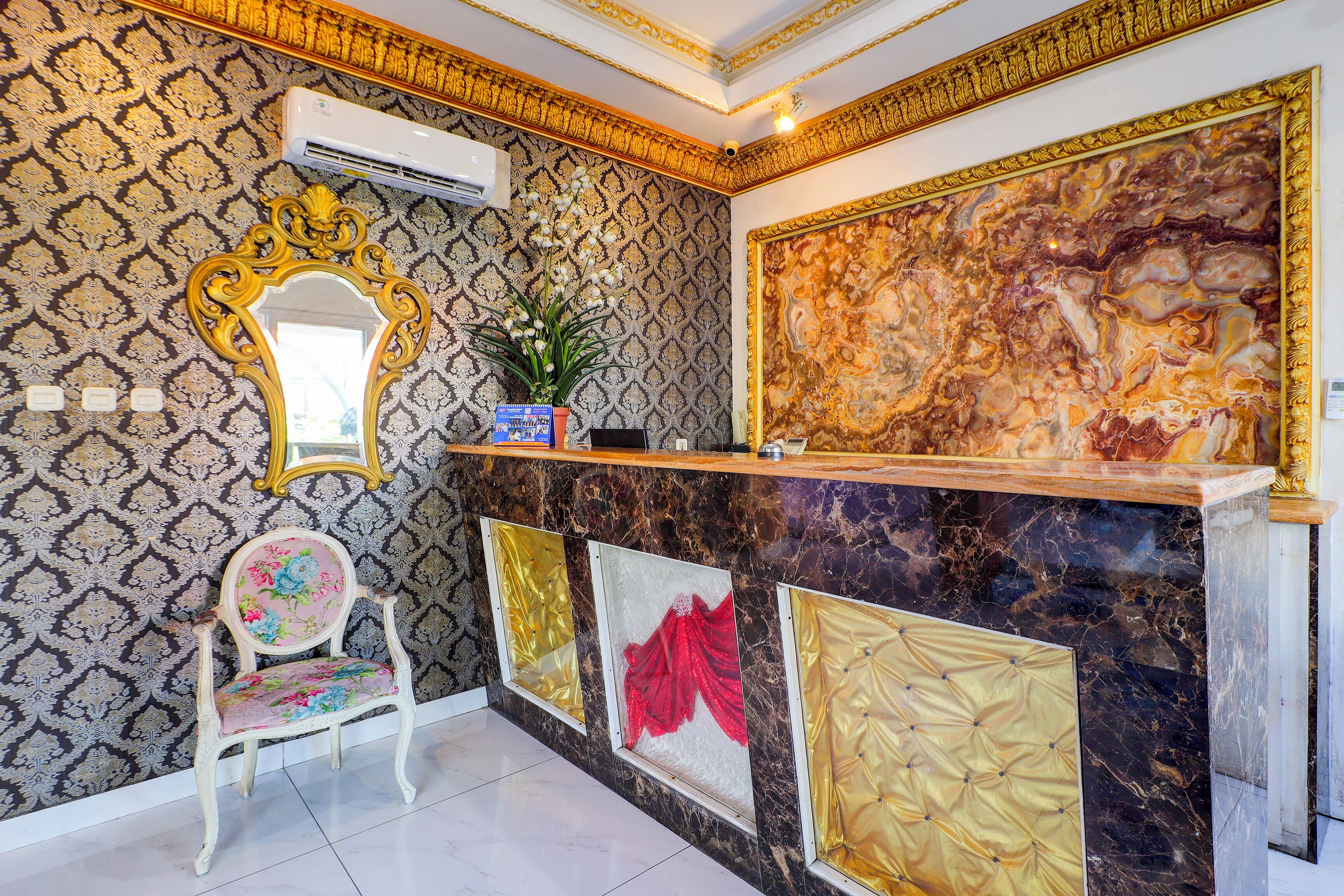 A reception area with a patterned wallpaper, a decorative mirror, a floral chair, and a marble reception desk.
