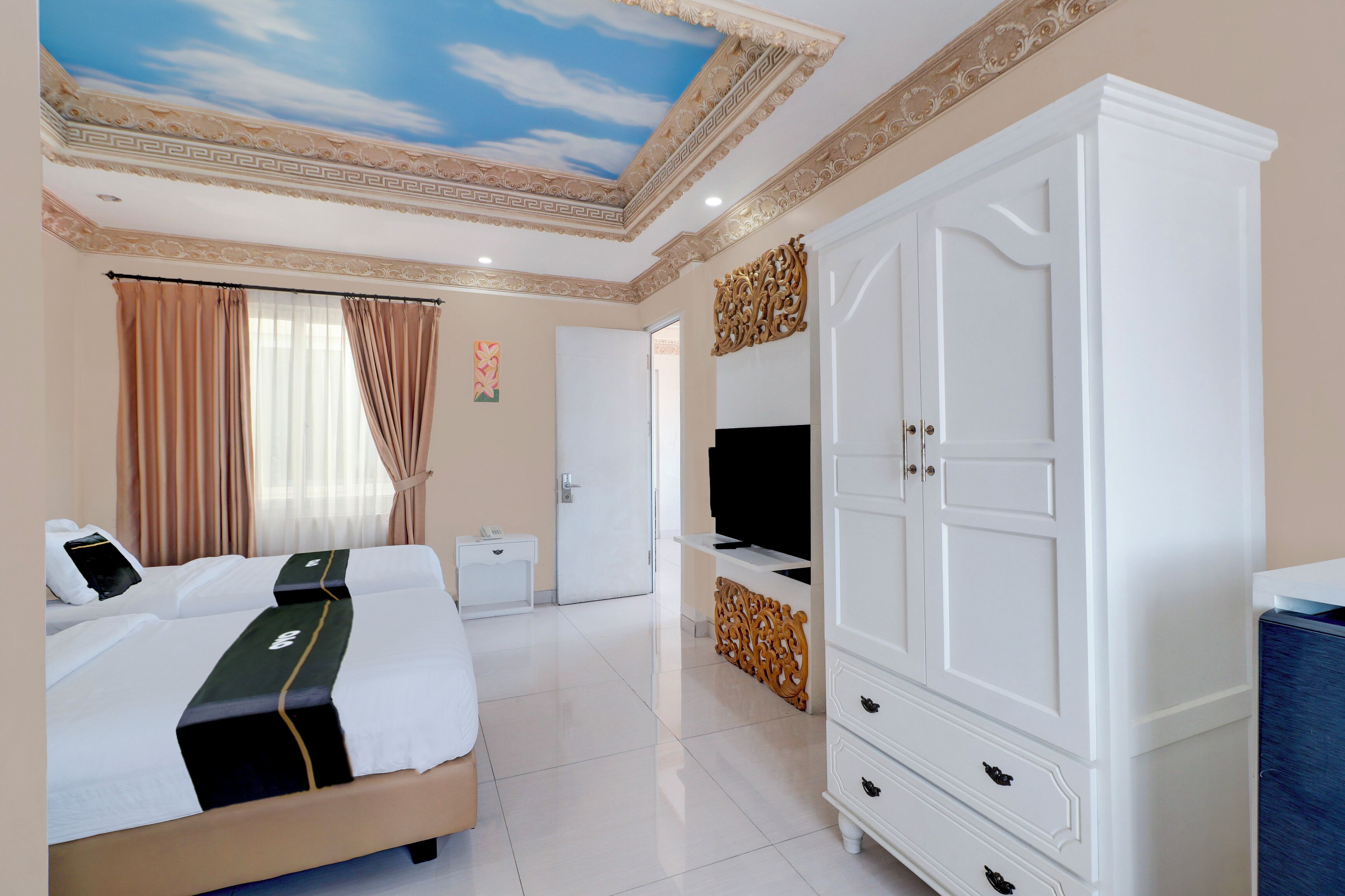 A hotel room with a bed, a wardrobe, a television, and a ceiling with a decorative design.