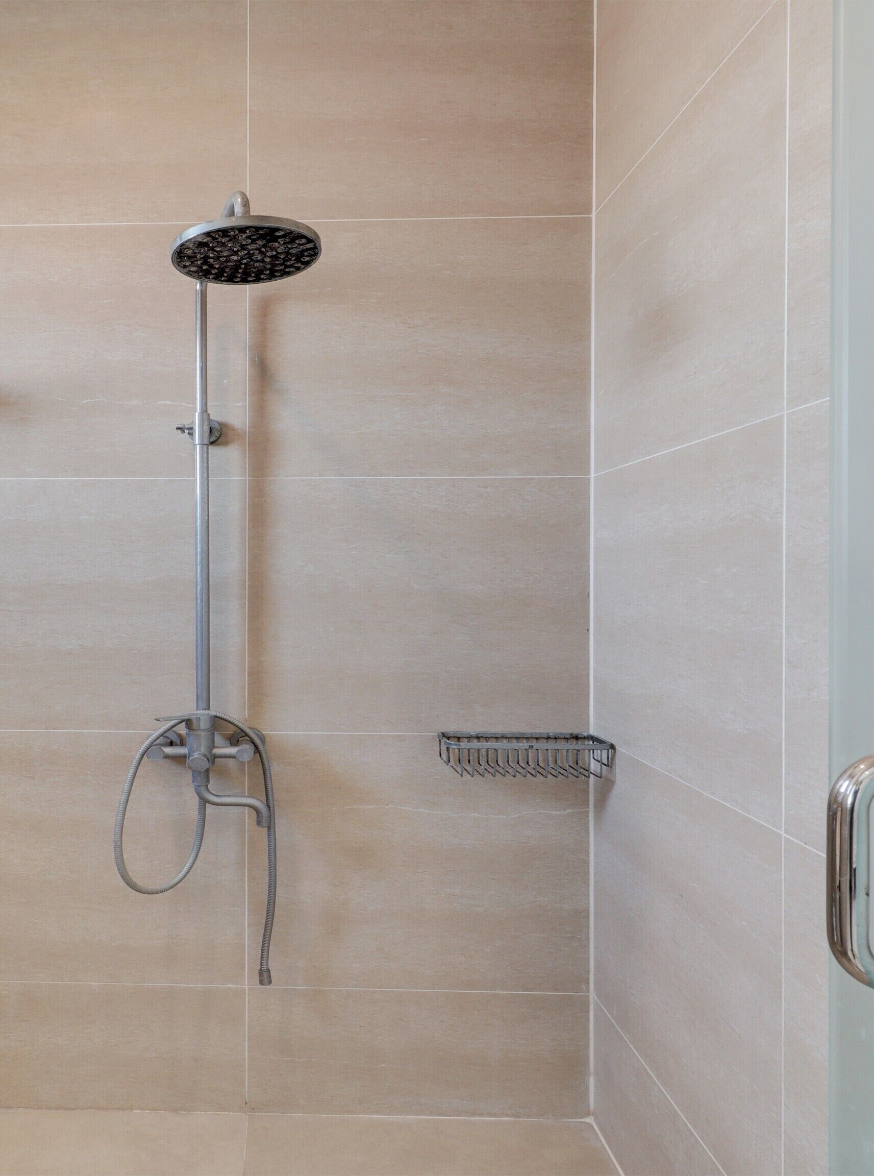 A shower with a handheld showerhead and a wall-mounted control.