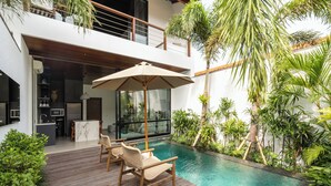 Ein moderner Poolbereich im Freien mit einer Holzterrasse, Liegestühlen und einer durch die Terrasse gut einsehbaren Küche.