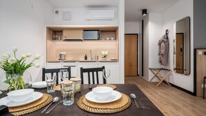 A modern kitchen with a microwave, sink, and wooden cabinets. There is a dining table set with plates, glasses, and a vase of flowers. - Apartamenty Sun & Snow Zamoyskiego (Warsaw)