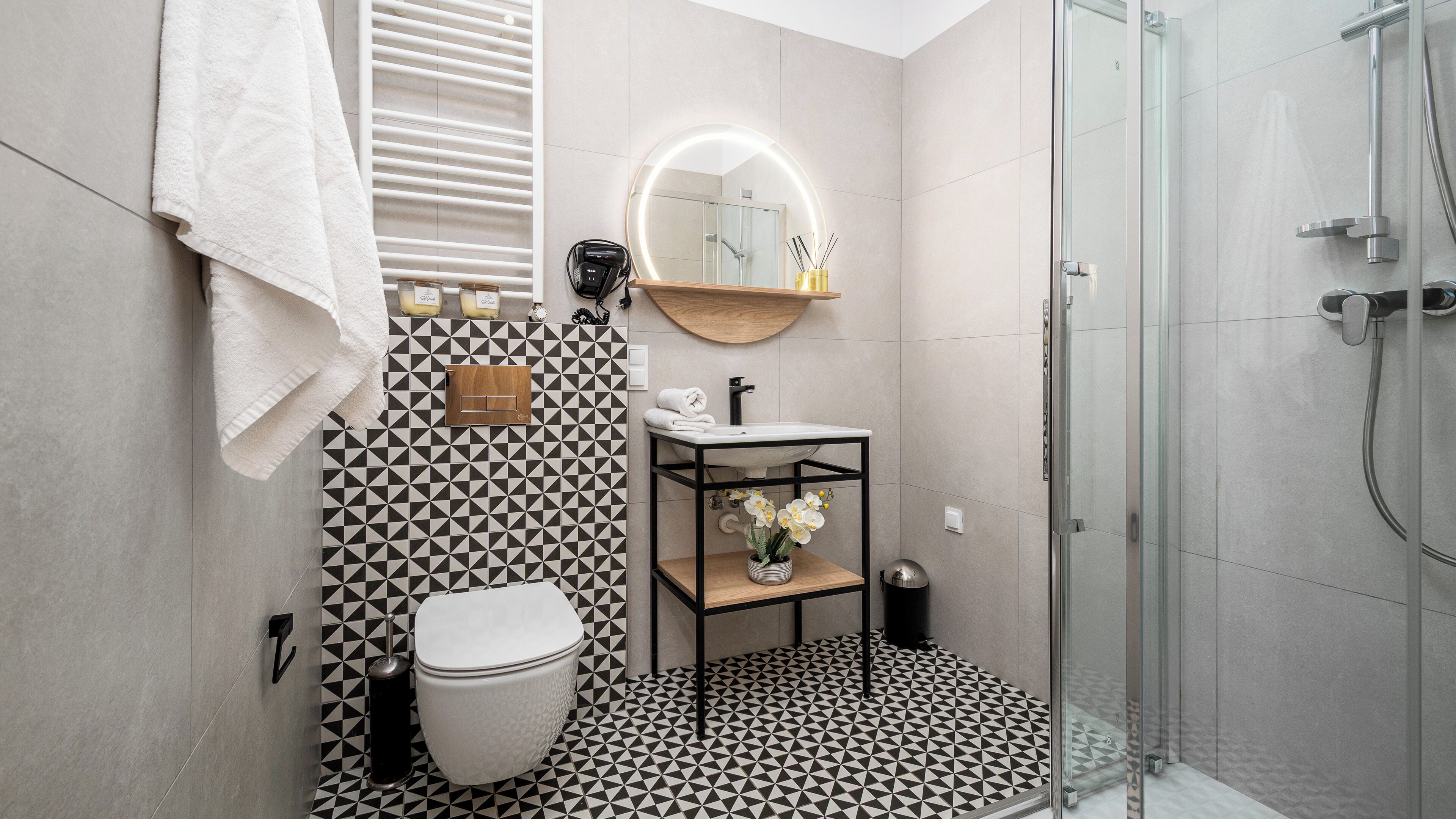 A modern bathroom with a black and white patterned floor, a white toilet, a sink with a mirror above it, and a glass shower enclosure.