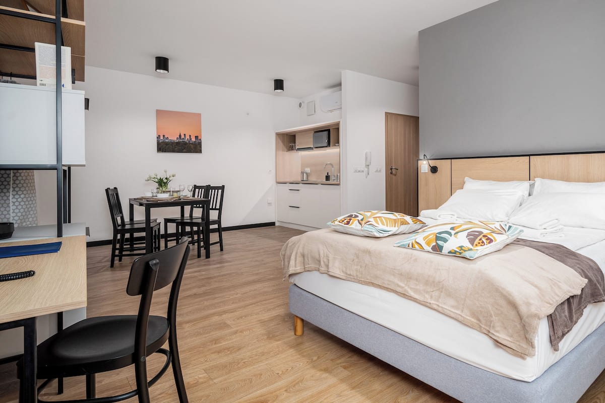 A modern hotel room with a bed, a desk, and a kitchenette.