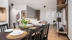 A modern hotel room with a dining area, a bed with white linens, a bedside table, and a large window with sheer curtains. - Apartamenty Sun & Snow Zamoyskiego (Warsaw)