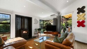 A modern living room with leather sofas, a glass coffee table, a fireplace, and a television. - Arrowtown Luxury Escape with Hot Tub & BBQ (Arrowtown)