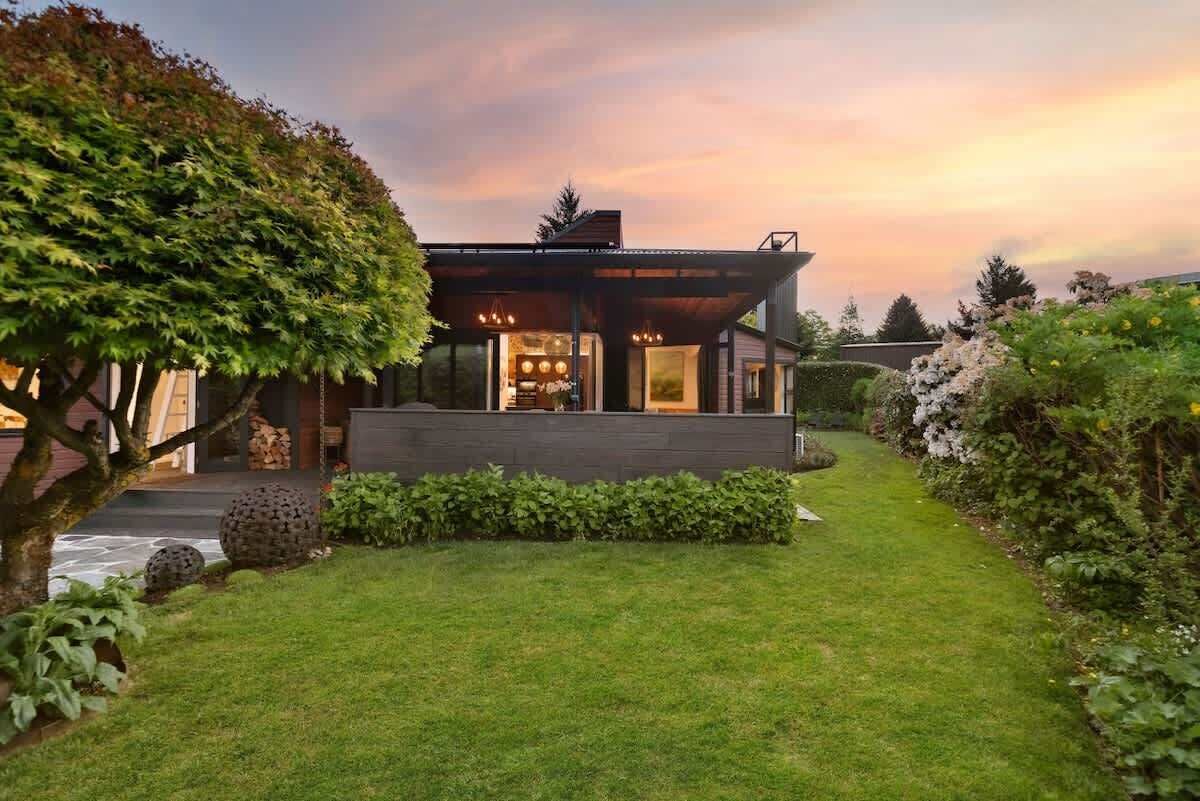 A modern house with a well-maintained garden, a clear sky, and a sunset.