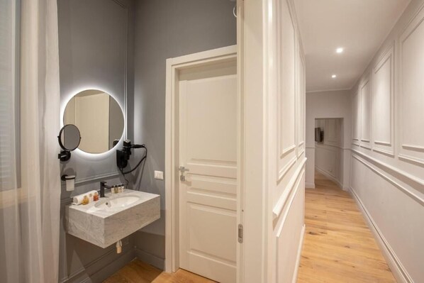 A modern bathroom with a marble sink, a round mirror with a light, and a white door. - Garden Palace (Rome)
