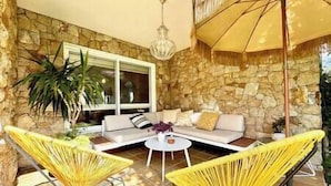 A sunlit patio with a stone wall, a white sofa, yellow chairs, and a table with a yellow umbrella. - Villa in Baiona YBH (Baiona)