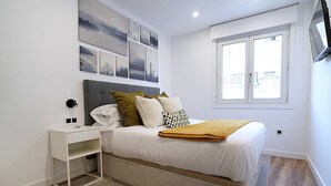 Un dormitorio con cama, mesita de noche y ventana.