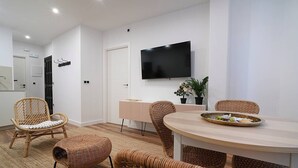 Una sala moderna con una mesa redonda de madera, sillas de mimbre, un televisor de pantalla plana en la pared y una pequeña planta en maceta.