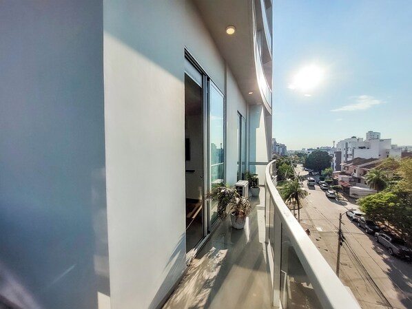 A modern building with large windows, a balcony with potted plants, and a view of a cityscape.