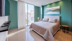 Un dormitorio moderno con una cama grande, un televisor, una mesita y un cuadro en la pared.