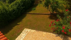 A garden with a tiled patio, green grass, and red flowers. - 3-bedroom apartment in village Vinkuran (Vinkuran)