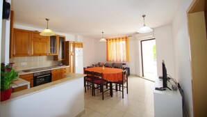 A modern kitchen with wooden cabinets, a dining table with chairs, and a TV in the living area. - 3-bedroom apartment in village Vinkuran (Vinkuran)