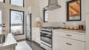 Een moderne keuken met witte kasten, roestvrijstalen apparatuur en grote ramen met uitzicht op een besneeuwd landschap.