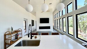 Een moderne keuken met een groot eiland, inbouwapparatuur en grote ramen met uitzicht op de omgeving.