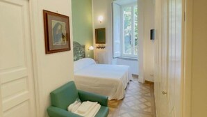 A hotel room with a bed, a chair, a window, and a door.