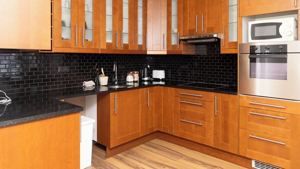 A modern kitchen with wooden cabinets, black backsplash, stainless steel appliances, and a white dishwasher. - Summerday Guesthouse (Reykjavík)