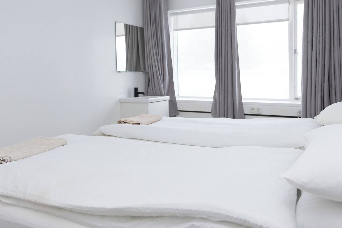 Een hotelkamer met twee bedden, een klein nachtkastje, een spiegel en een raam met gordijnen.