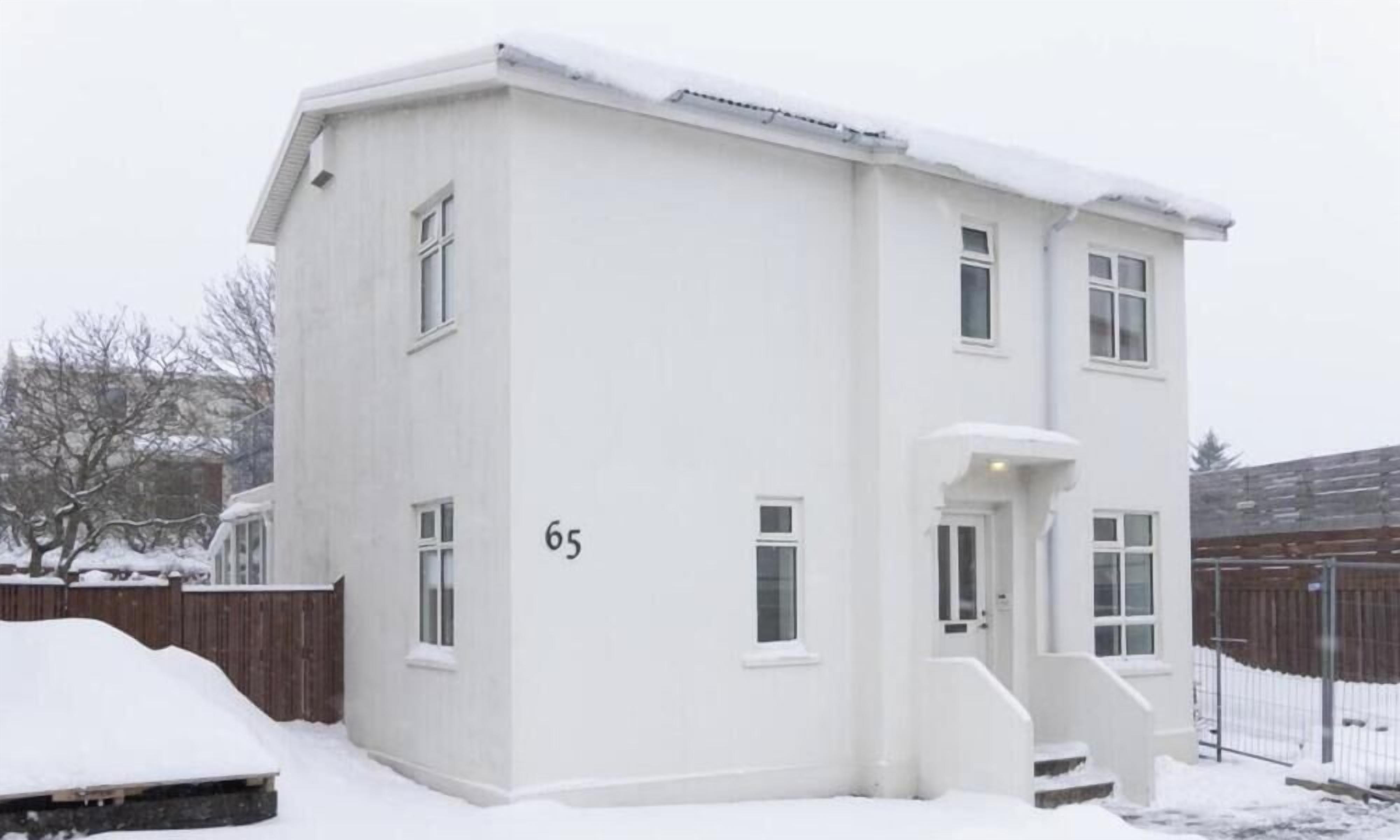 A white two-story building with a flat roof, number 65, and a small porch with steps.