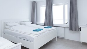 A white room with a bed, a window with curtains, and a radiator. - Summerday Guesthouse (Reykjavík)