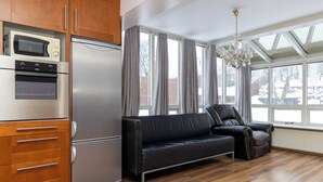 A modern kitchen with a built-in oven, microwave, and refrigerator. There is a black leather sofa and a chandelier. - Summerday Guesthouse (Reykjavík)
