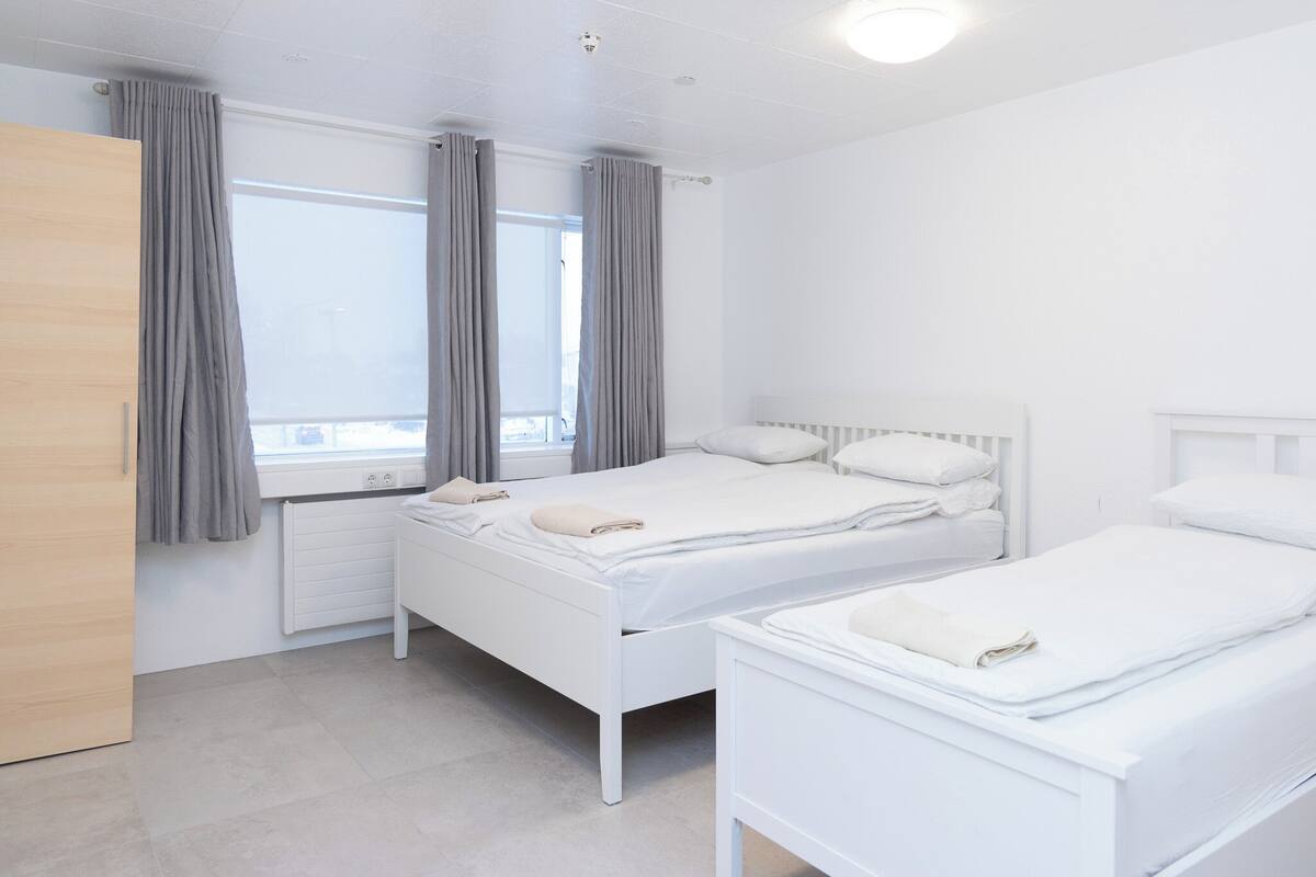 Een hotelkamer met twee bedden, een houten kledingkast en een raam met gordijnen.