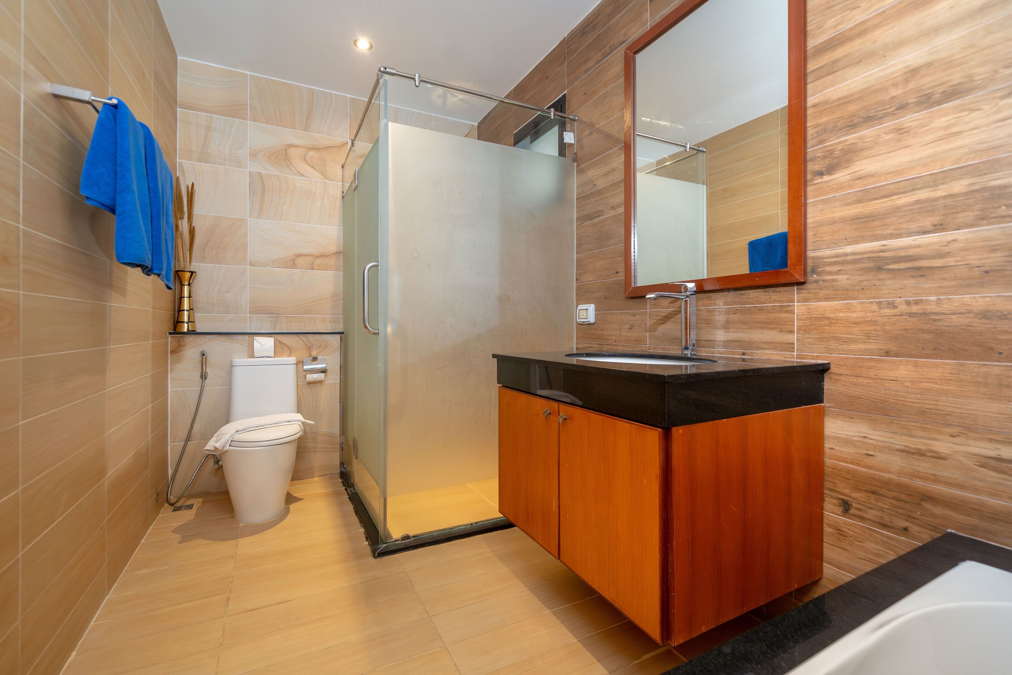 Une salle de bain moderne avec une douche à l’italienne en verre, un meuble-lavabo en bois et un grand miroir.