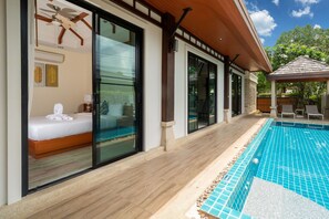 Ein modernes Hotelzimmer mit einer großen Schiebeglas-Tür, einem Deckenventilator und Blick auf den Swimmingpool.