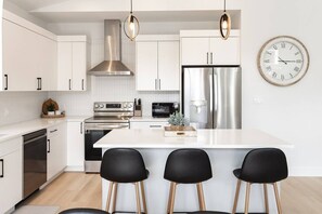 Une cuisine moderne avec des meubles blancs, des appareils en acier inoxydable, un îlot central doté de tabourets et une horloge murale.