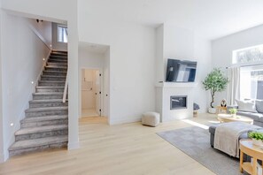 Un salon moderne avec un escalier, une cheminée, un téléviseur à écran plat et une grande fenêtre.