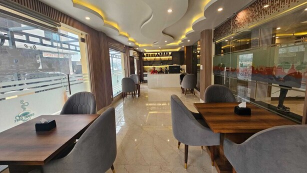 A modern cafe with a central counter, seating area with tables and chairs, and large windows offering views of the street. - Little Buddha Hotel Pvt. Ltd (Lumbini)