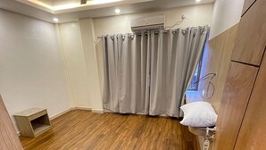 A room with a wooden floor, a ceiling fan, an air conditioning unit, and a window with curtains. - Little Buddha Hotel Pvt. Ltd (Lumbini)