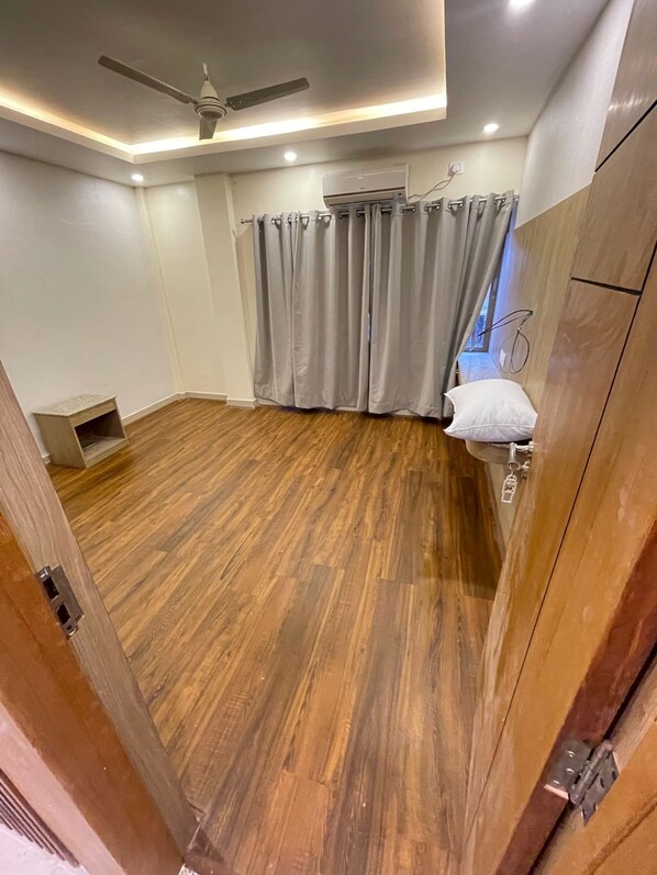 A room with a wooden floor, a ceiling fan, an air conditioning unit, and a window with curtains. - Little Buddha Hotel Pvt. Ltd (Lumbini)